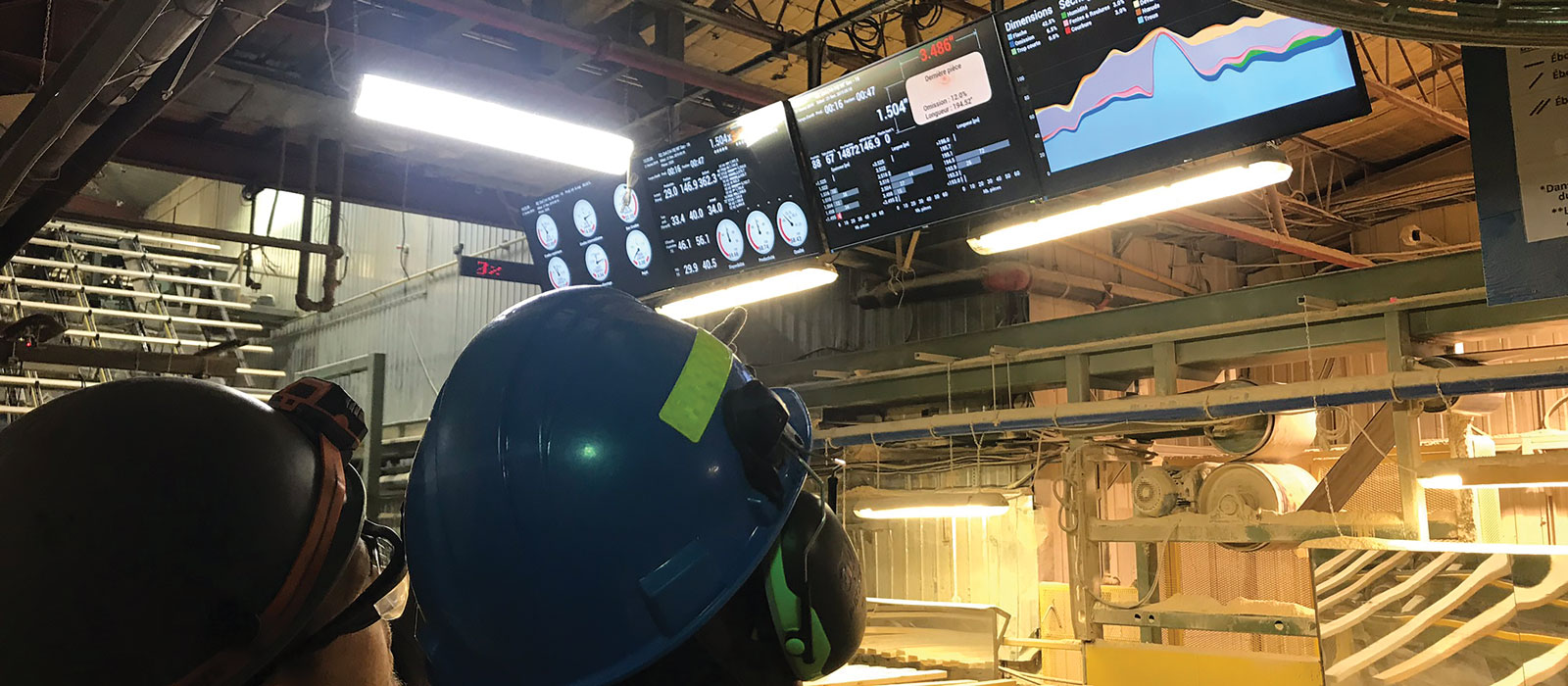 Mill workers consulting PMP TeamMate dashboards on the planer mill floor